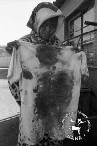 Mrs Mazibuko holds the bloody t-shirt of her son who was shot and killed by police, June 1985. Archived as SAHA collection AL3274_C26.2